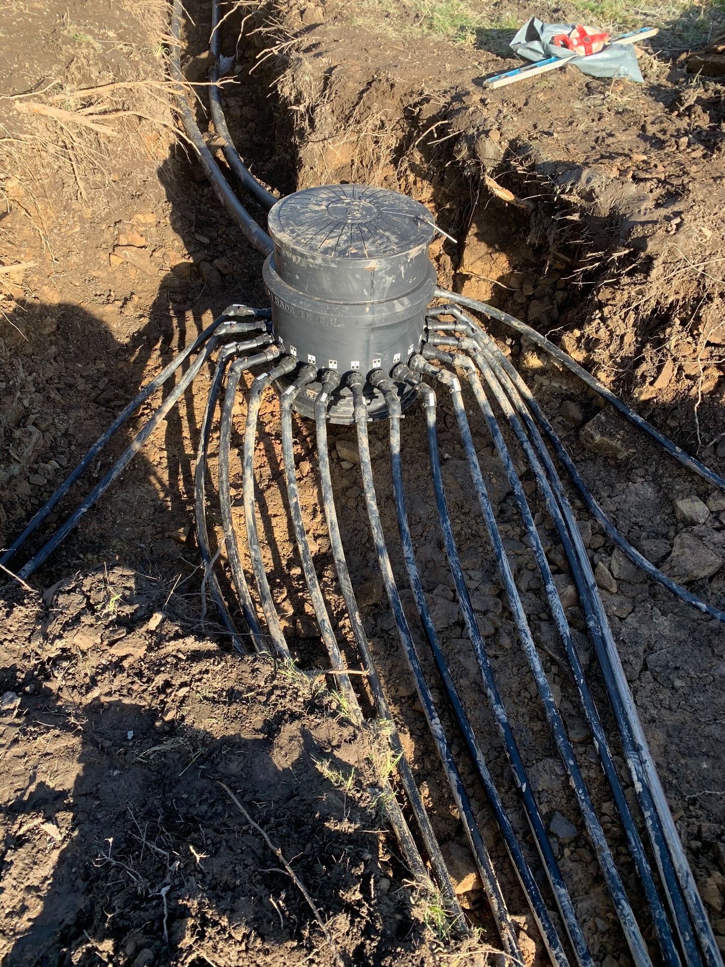 Ground array manifold header with loop pipes fanning into an open trench