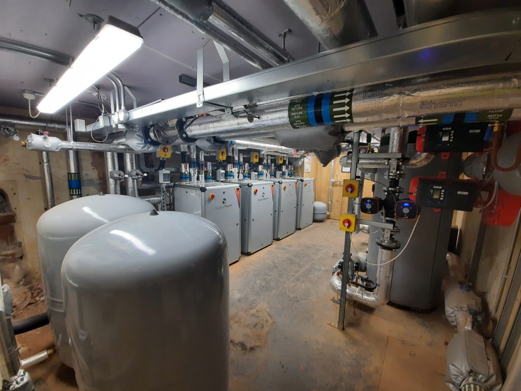 Commercial plant room with a row of MasterTherm heat pumps, buffer tanks and insulated pipework